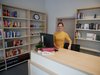 Zu sehen ist eine Frau an einem Tresen. Hinter ihr stehen Regale mit Büchern.