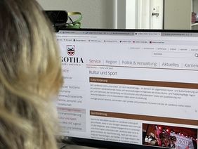 Zu sehen ist eine Person, die vor einem Bildschirm sitzt. Auf dem Bildschirm ist die Website des Landratamtes Gotha zu sehen.