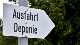 Zu sehen ist ein Schild in Form eines Pfeils auf dem "Ausfahrt Deponie" zu lesen ist. Der Pfeil zeigt nach links.