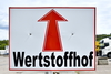 Zu sehen ist ein großes Schild auf dem ein roter Pfeil abgebildet ist. Darunter steht die Aufschrift Wertstoffhof in Schwarz.