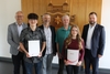 Die sechs Personen stehen in einem Beratungsraum des Landratsamtes. Sie stehen vor einem großen Landkreiswappen aus Holz, das an der Wand angebracht ist.