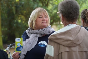 Eine Frau mit blonden Haaren hält einen Flyer in der Hand, auf dem "AGATHE" steht. Mit dem Rücken zur Kamera steht eine weitere Frau.