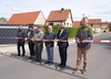 Zu sehen ist ein rot-weißes Flatterband, das über eine Straße gespannt ist. Dahinter stehen fünf Männer und eine Frau mit Scheren in der Hand, die das Band zerschneiden.