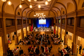 Zu sehen ist ein großer mit Menschen gefüllter Saal. 