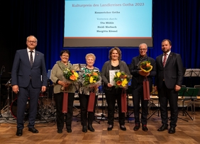 Zu sehen sind 6 Personen auf einer Bühne. Die vier Personen in der Mitte halten Blumensträuße in den Händen. Ihnen wurde der Kulturpreis überreicht. Im Hintergrund auf einer Leinwand ist zu lesen: "Kulturpreis des Landkreises Gotha 2023".