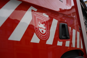 Zu sehen ist ein Teil reines roten Feuerwehr-Einsatzwagens. Darauf ist eine Folierung mit dem einem weißen Wappen bzw. Logo. 