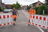 Zu sehen sind zwei Männer, Ringo Frommann und Rainer Kreidel, in Arbeitskleidung. Sie stehen auf einer Straße und öffnen Bauzäune.