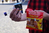 Zu sehen ist eine Nahaufnahme von den Händen einer Person. Sie hält eine Tüte Gummibärchen, Alkohol und eine Schachtel Zigaretten.