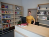 Zu sehen ist eine Frau an einem Tresen. Hinter ihr stehen Regale mit Büchern.