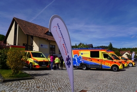 Zu sehen ist ein weißes Gebäude. Davor stehen Rettungswagen. Der Himmel im Hintergrund ist blau.