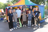Zu sehen ist ein kleines Zirkuszelt. Davor stehen Kinder und Erwachsene mit Utensilien aus dem Zirkus. Dazu gehören ein Einrad, Jonglierkeulen und vieles mehr. 