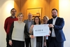 Zur Scheckübergabe wurde ein Foto mit allen Beteiligten im Landratsamt vor einem großen hölzernen Landkreiswappen gemacht. Den Scheck halten die Leiterin des Frauenhauses Anja Wild (mittig) und Landrat Onno Eckert (rechts) in der Hand.