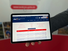 Ein Tablet wird ins Bild gehalten. Darauf ist die Website der Kreisvolkshochschule zu sehen.