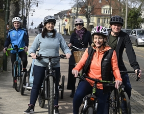 Zu sehen sind fünf Personen auf Fahrrädern. Sie tragen Fahrradhelme und lächeln in die Kamera.