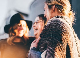 Drei Frauen unterhalten sich. Sie stehen nebeneinander und lächeln dabei.