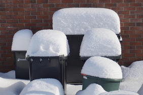 Eine Reihe Mülltonnen, die mit Schnee bedeckt sind.