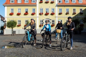 Zu sehen sind vier Personen auf Fahrrädern vor dem Rathaus.